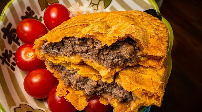 Golden-crusted meat pie, cut open to reveal savory filling, served with cherry tomatoes and rice.