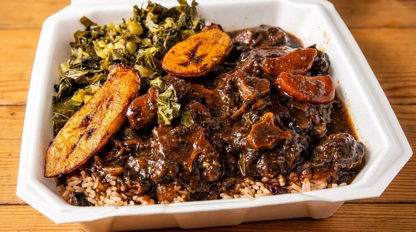 Oxtail stew with rice, collard greens, and fried plantains in a white takeout container.