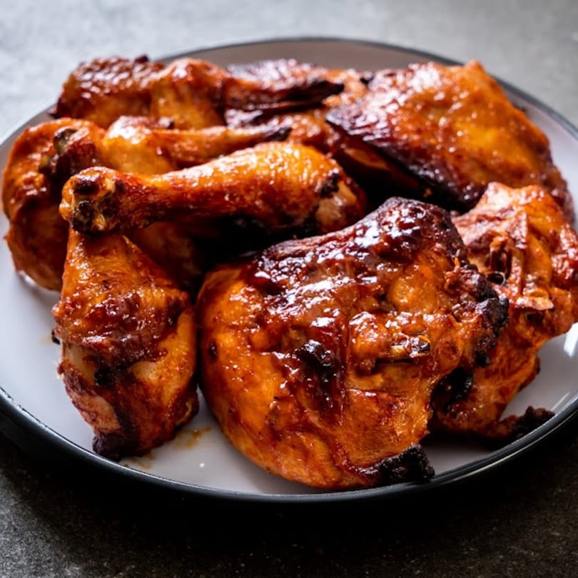 A plate of Caribbean-style grilled chicken pieces with a glossy, dark brown glaze.